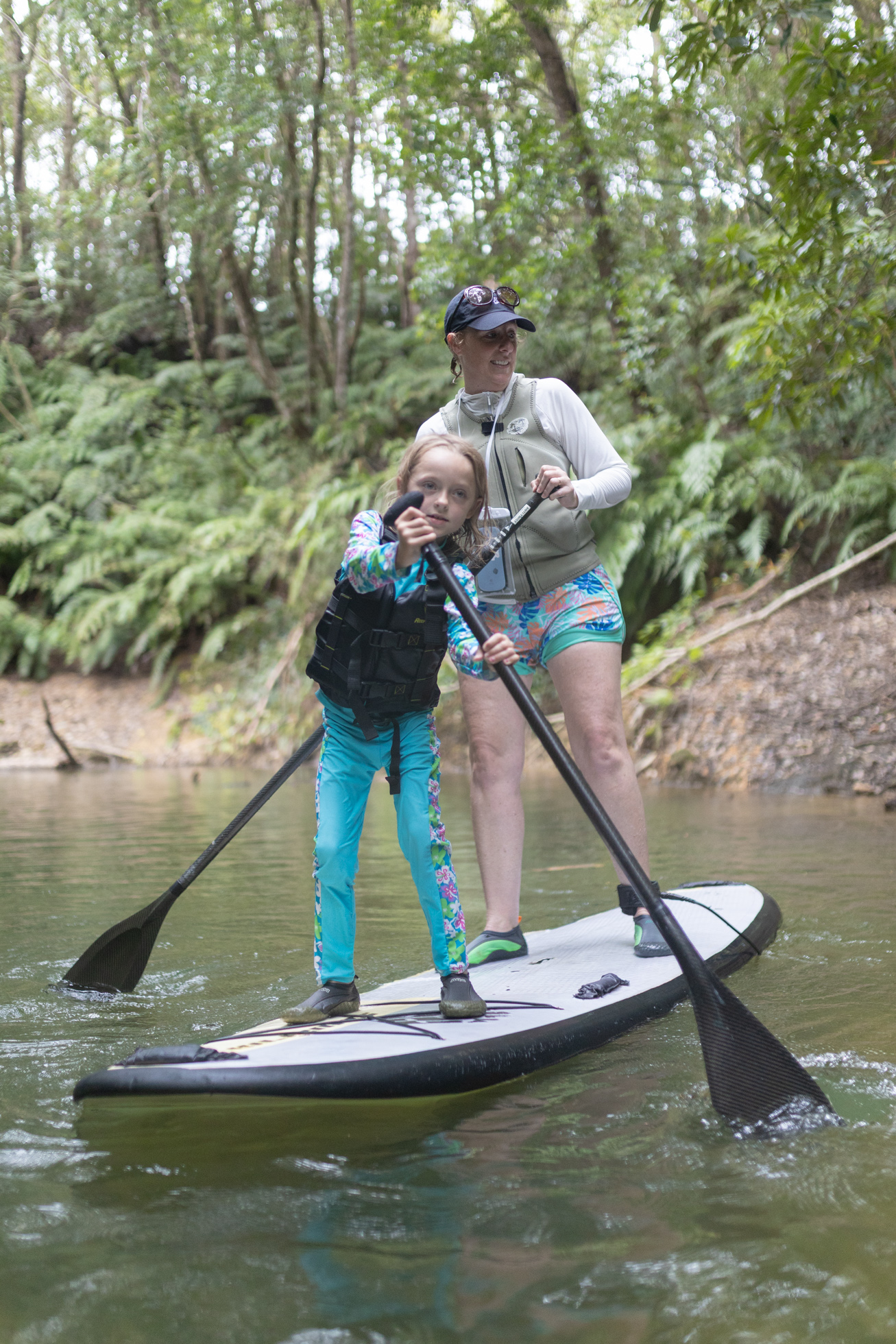 A woman and child paddleboarding together on a forest river